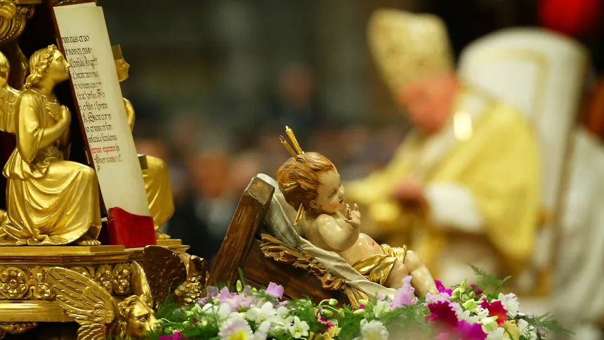 Statue av Jesusbarnet med pave Johannes Paul II på en stol i bakgrunnen